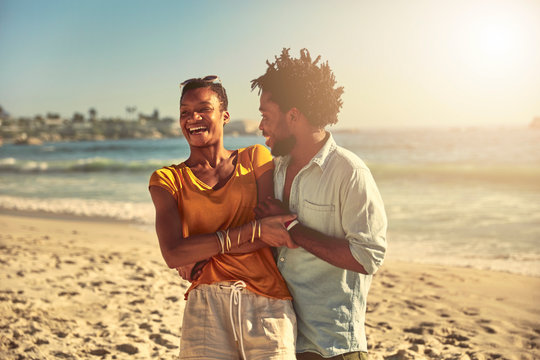 Playful young couple hugging and laughing on sunny summer ocean beach