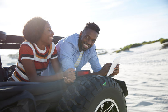 Smiling young couple using digital tablet in jeep on sunny beach
