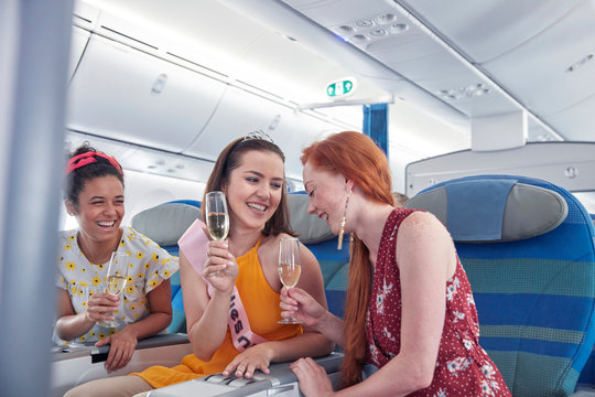 Young women friends laughing, drinking champagne in first class on airplane