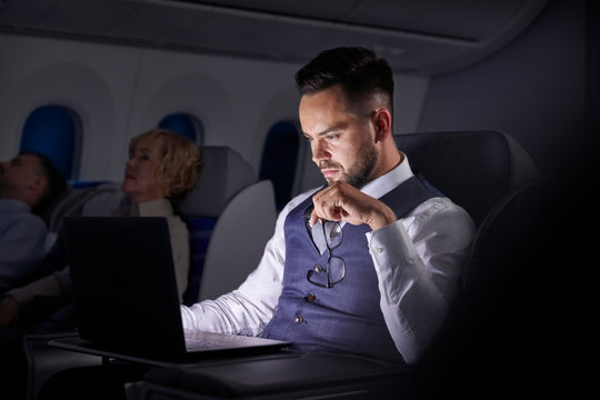Serious businessman working at laptop on overnight airplane