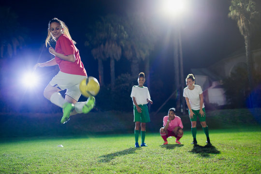Young female soccer players practicing on field at night, doing back kick
