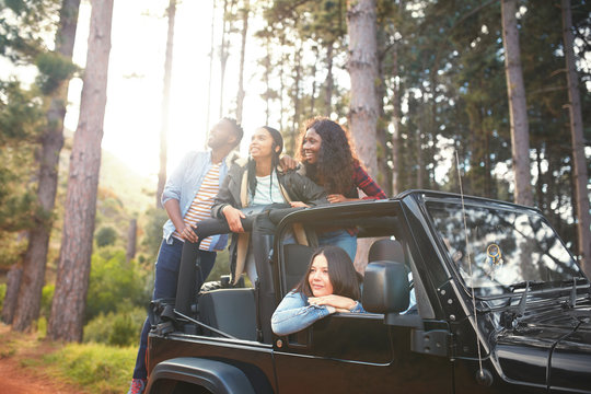 Young friends in jeep looking up at trees in woods, enjoying road trip