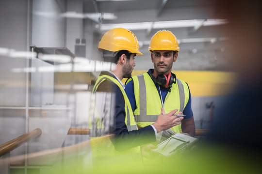 Male supervisor and worker with clipboard talking in factory