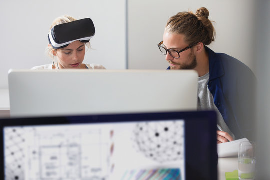 Focused computer programmers programming virtual reality simulator glasses at computer in office