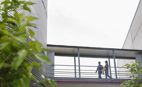 Supervisors walking on elevated walkway between factory buildings
