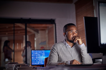 Serious, focused businessman headphones working late at computer in dark office at night