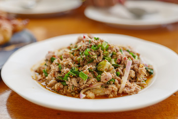 Close up view of Larb, Thai Spicy minced pork or duck salad, on wooden table and blur background of another dish.