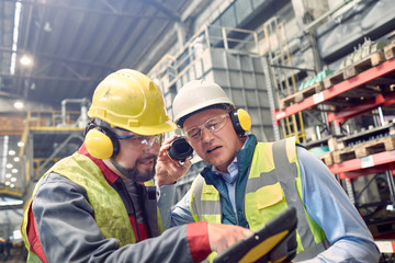 Steelworkers wearing ear protectors using digital tablet in steel mill