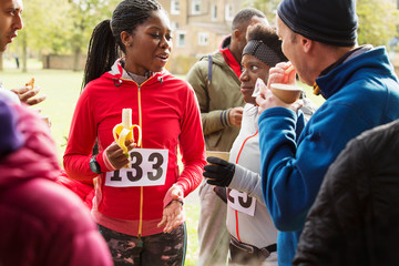 Runners drinking water and eating banana at charity race in park