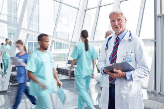 Portrait Confident Male Doctor With Clipboard In Busy Hospital Lobby