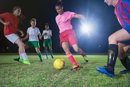 Young female soccer players playing soccer on field at night