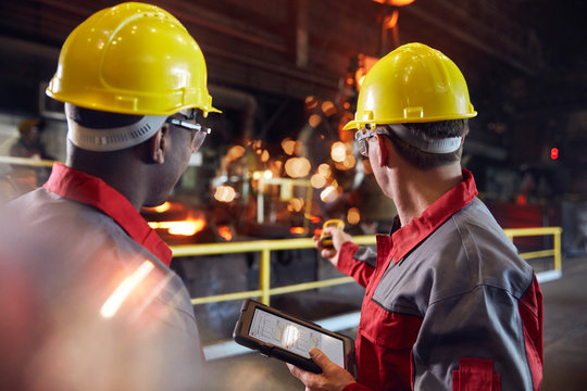Supervisor and steel worker with digital tablet working in steel mill