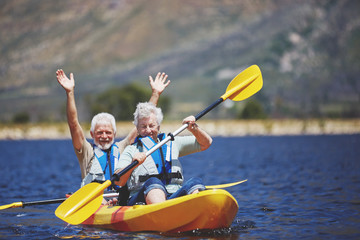 Playful, energetic active senior couple kayaking on sunny summer lake