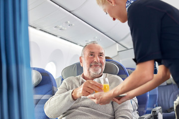 Flight attendant serving orange juice to man on airplane