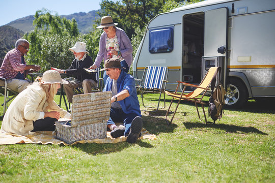 Active senior friends enjoying picnic outside camper van at sunny summer campsite