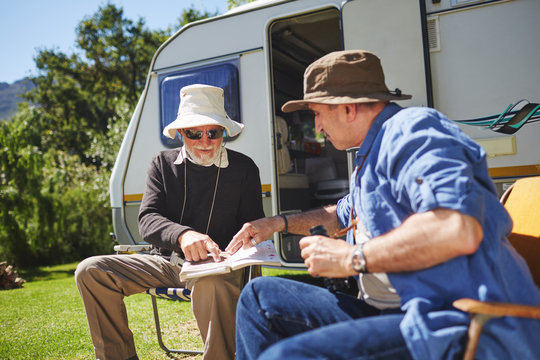 Senior men friends looking at guidebook outside camper van at sunny summer campsite