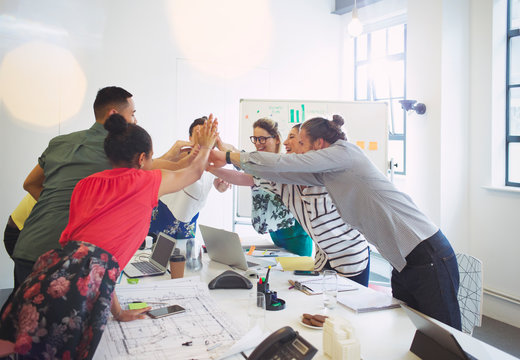 Enthusiastic architects high-fiving in conference room meeting