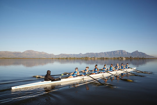Female rowers rowing scull on sunny lake under blue sky