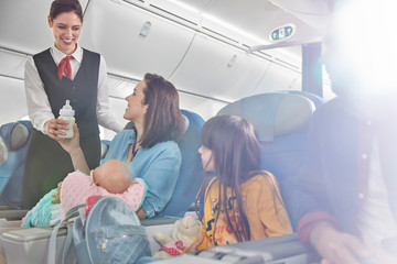 Smiling flight attendant bringing baby bottle to mother baby on airplane