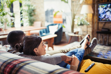 Affectionate young couple watching TV on living room sofa