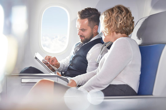 Businessman and businesswoman using digital tablet on airplane