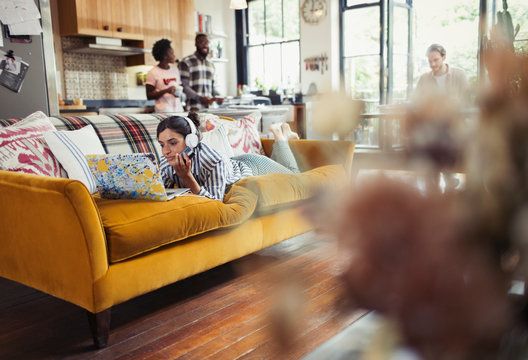 Young Woman With Headphones Using Laptop On Living Room Sofa