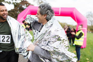 Smiling male marathon runners finishing race, wearing thermal blankets