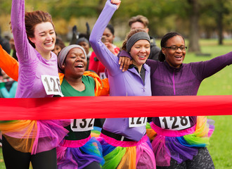 Women friend runners in tutus running, crossing charity run finish line