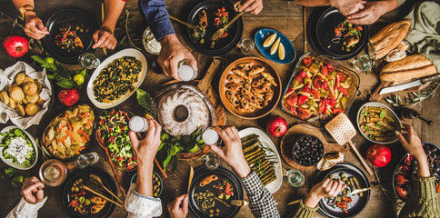 Traditional Turkish celebration dinner. Flat-lay of people eating Turkish salads, cooked vegetables, meze starters, pastries and drinking raki drink, top view, wide composition. Middle Eastern cuisine - obrazy, fototapety, plakaty