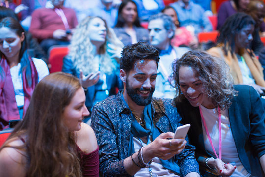 Smiling business people using smart phone in conference audience