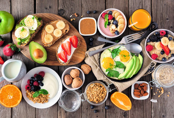 Healthy breakfast table scene with fruit, yogurts, oatmeal, smoothie, nutritious toasts and egg skillet. Top view over a wood background. - obrazy, fototapety, plakaty