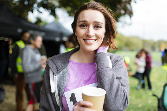 Portrait smiling female marathon runner drinking water in park