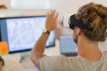 Computer programmer testing virtual reality simulator glasses at computer in office