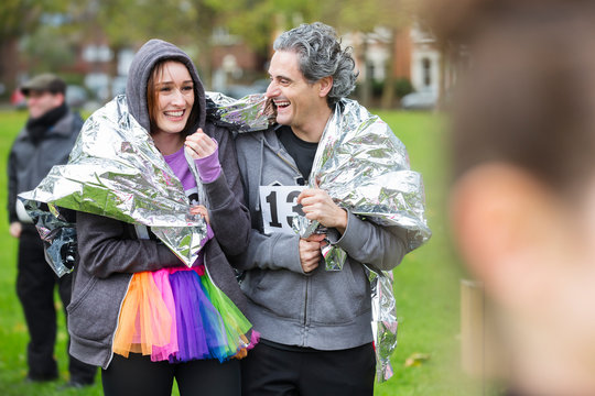 Happy couple runners wrapped in thermal blanket at charity run in park