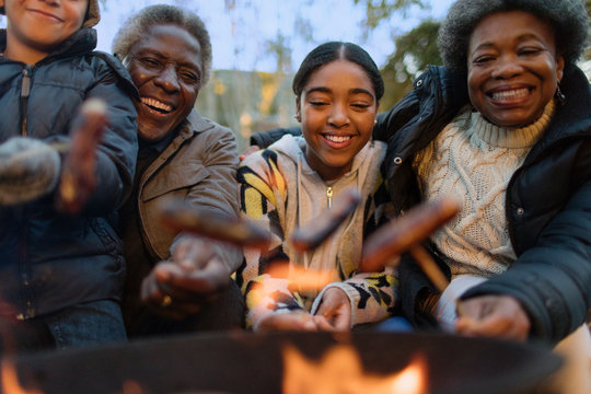 Happy grandparents and grandchildren roasting hot dogs over campfire