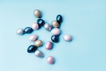 Colored painted pearl chicken and quail eggs of pink, silver, golden and blue color on a light blue pastel background. Minimalistic creative classic easter festive flat lay. Copyspace for text
