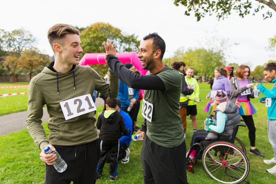 Male runner friends high-fiving after charity run in park