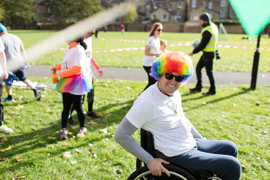 Portrait smiling, playful man in wheelchair wearing clown wig at charity race in sunny park