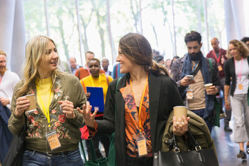 Women friends with coffee walking and talking, arriving at conference