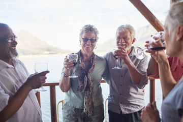 Happy active senior friends drinking wine on balcony