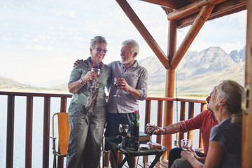 Happy active senior couples drinking wine on summer balcony