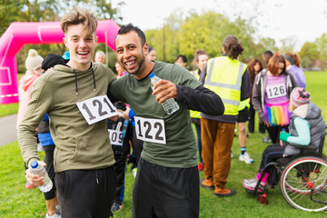 Portrait enthusiastic male runner friends water hugging at charity run finish line in park