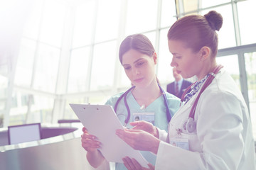 Female doctor nurse consulting, reviewing medical record on clipboard in hospital