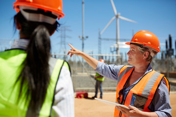 Female engineer digital tablet talking to colleague at wind turbine power plant