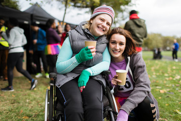 Portrait smiling woman in wheelchair friend, drinking water at charity race in park
