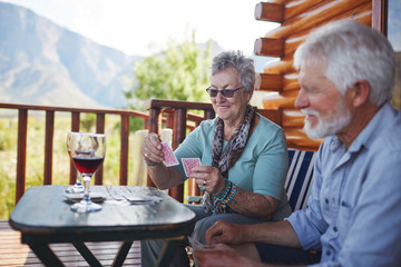 Active senior couple drinking wine and playing cards on cabin balcony