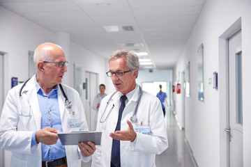 Male doctors clipboard making rounds, talking in hospital corridor