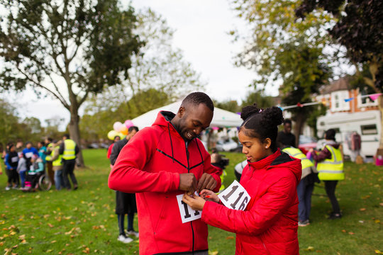Daughter pinning marathon bib on father runner at charity run in park