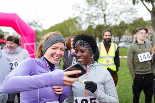 Female runner friends using smart phone at charity run in park