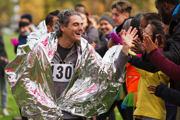 Enthusiastic male marathon runner in thermal blanket high-fiving spectators